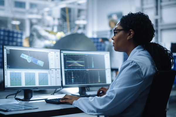 Woman engineer using computer to analyze satelite and other mathematical diagrams.